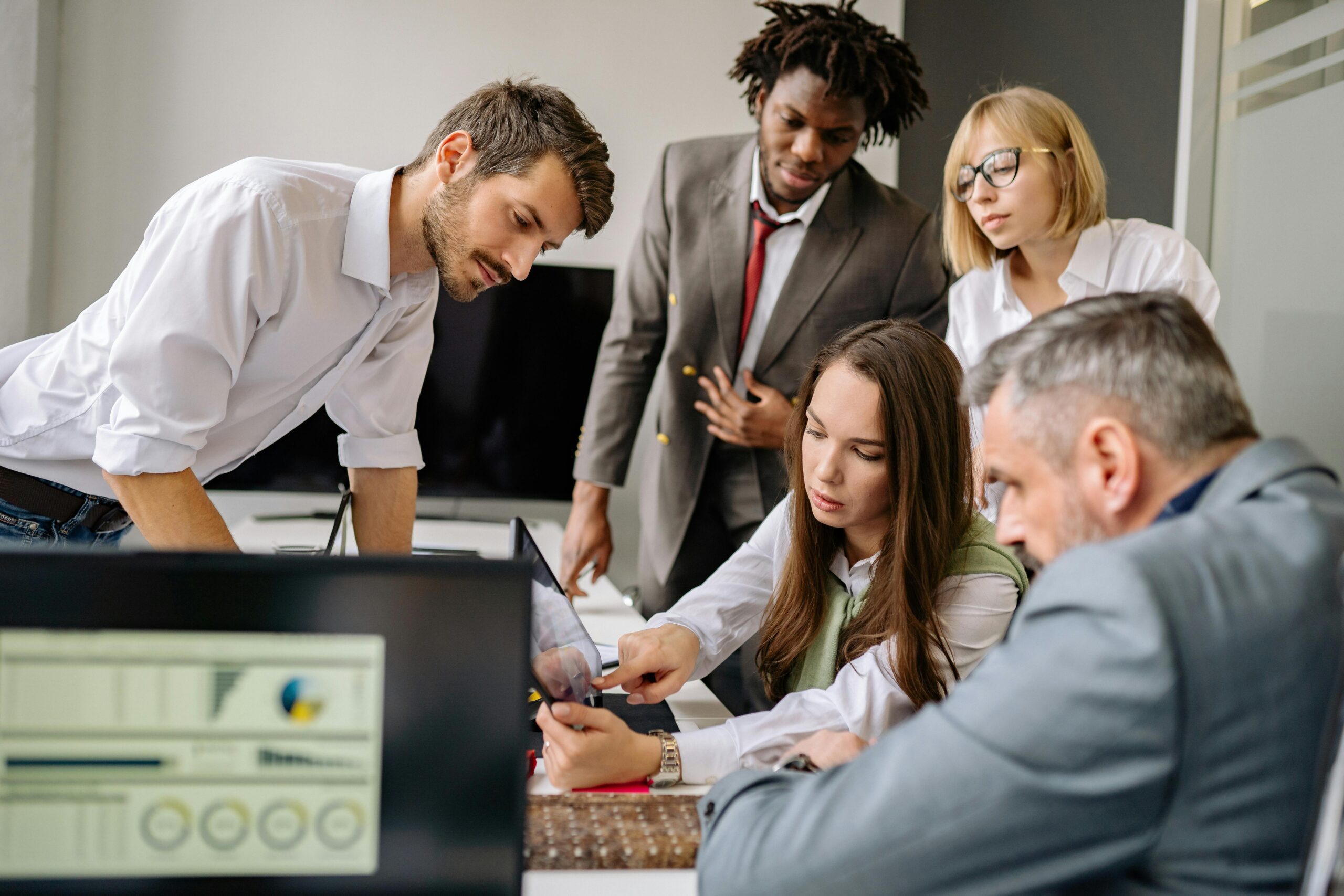 Home 5 A diverse team engages in a collaborative meeting in a modern office setting, focused on digital analysis.